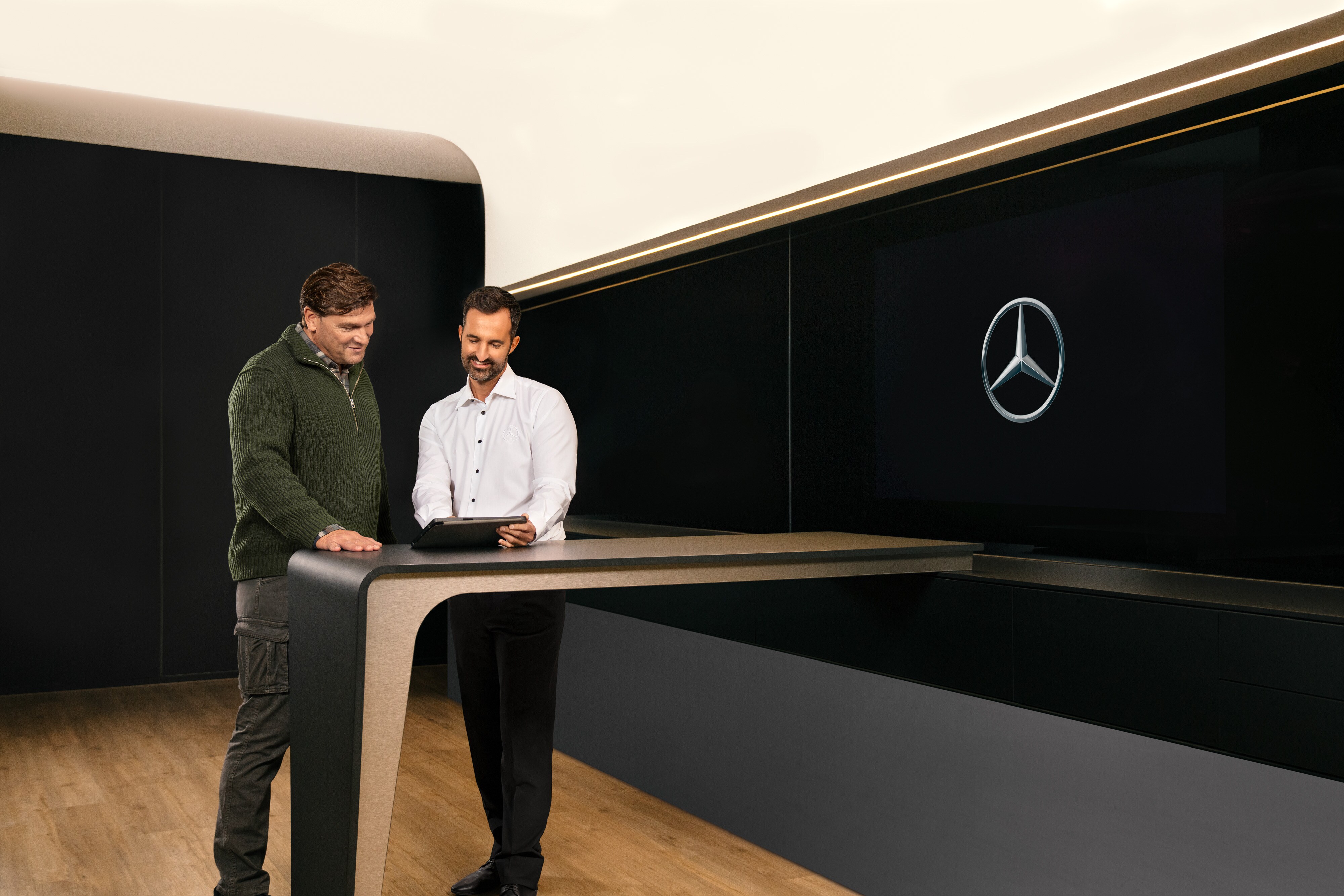 Mercedes-Benz | ServiceCare veículos comerciais ligeiros Dois homens numa consulta, de pé à volta de uma mesa, a olhar para um iPad.