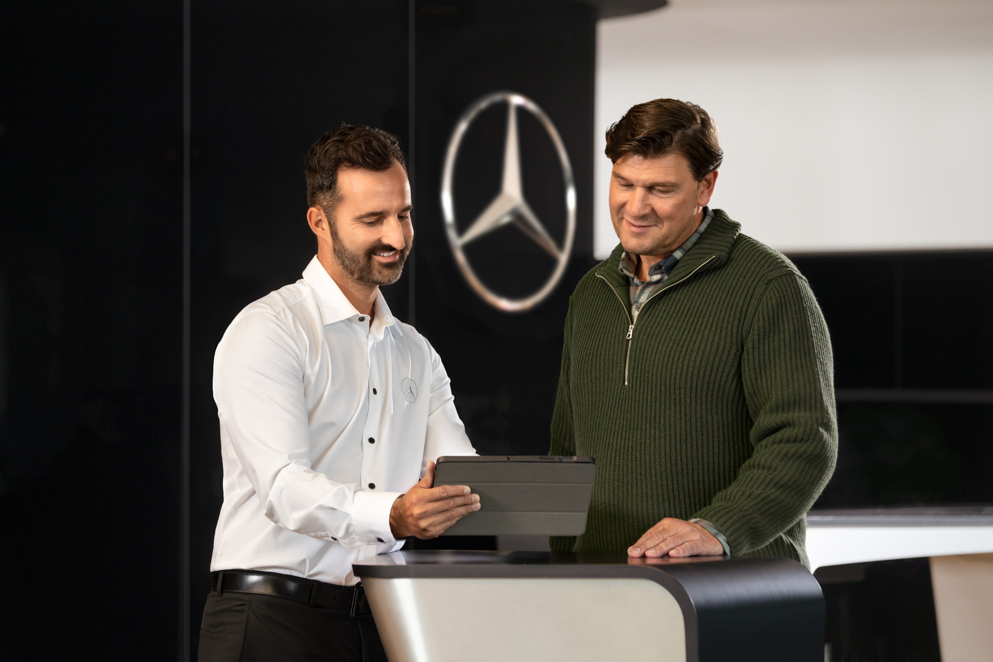 Mercedes-Benz | Visão geral dos serviços Dois homens a conversar num balcão, enquanto olham para um tablet, em frente à estrela da Mercedes-Benz.